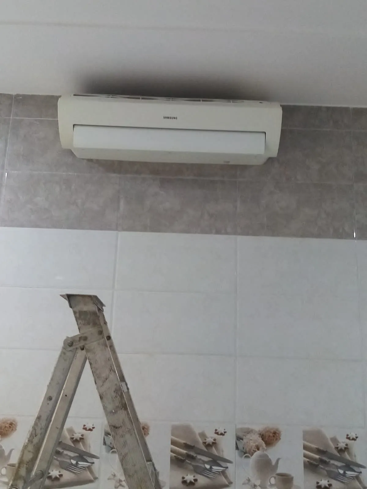 صيانة مكيفات سامسونج: مكيف سبليت فوق جدار مبلط وسلم ألمنيوم وأدوات على الأرض